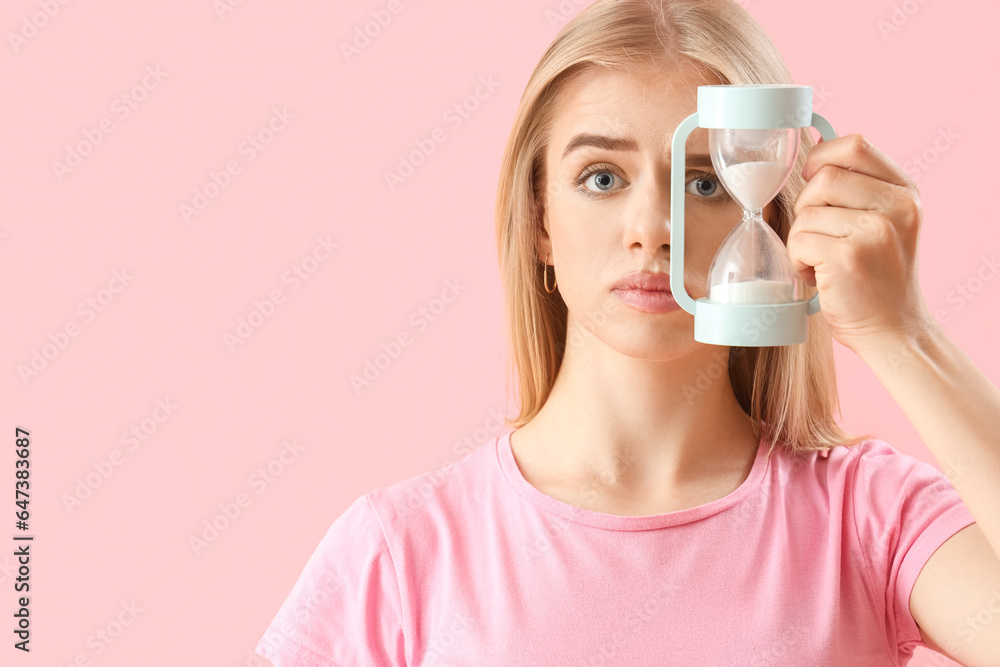 Stressed young woman with hourglass on pink background, closeup. Deadline concept