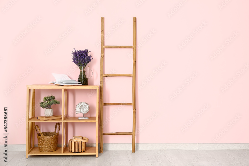 Jug with beautiful lavender flowers, decor and ladder near pink wall in room