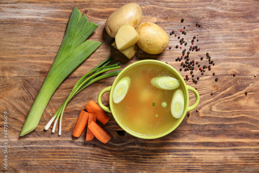 Pot of tasty vegetable broth with ingredients on wooden background