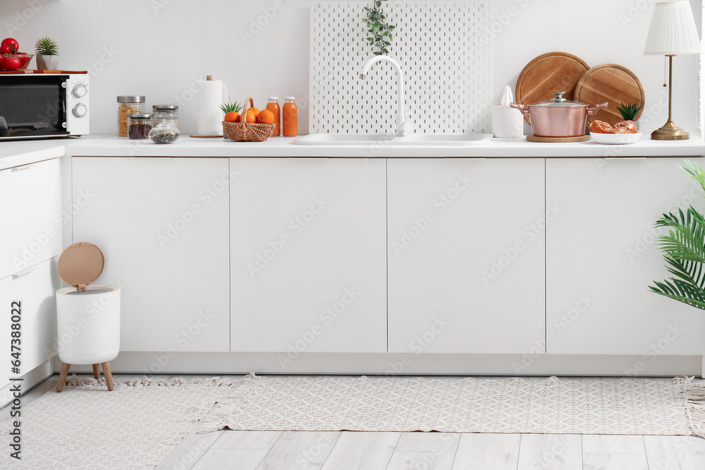 Interior of modern kitchen with stylish rug, trash bin and white counters