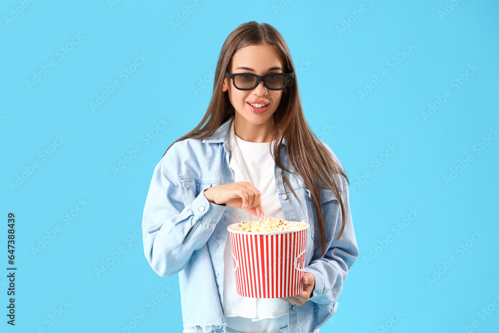 Young woman in 3D glasses with popcorn watching movie on blue background