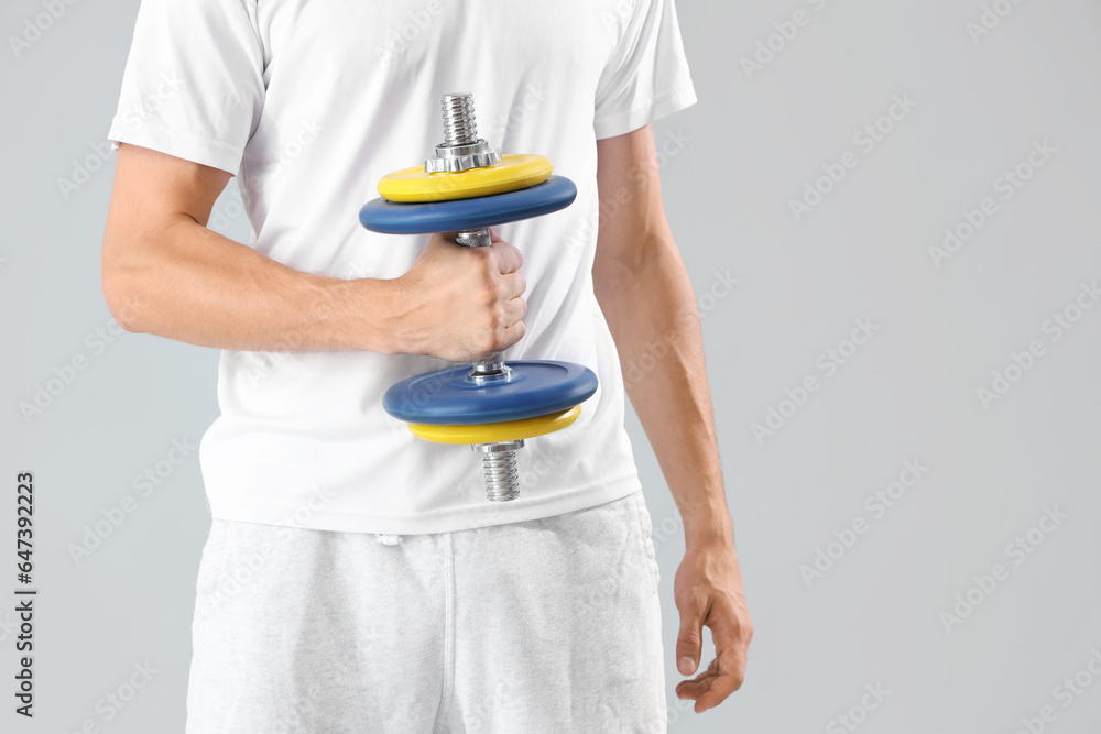 Young man with dumbbell on grey background