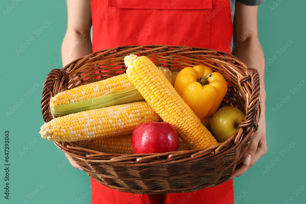 Beautiful young female farmer with wicker basket full of ripe vegetables and fruits on green backgro