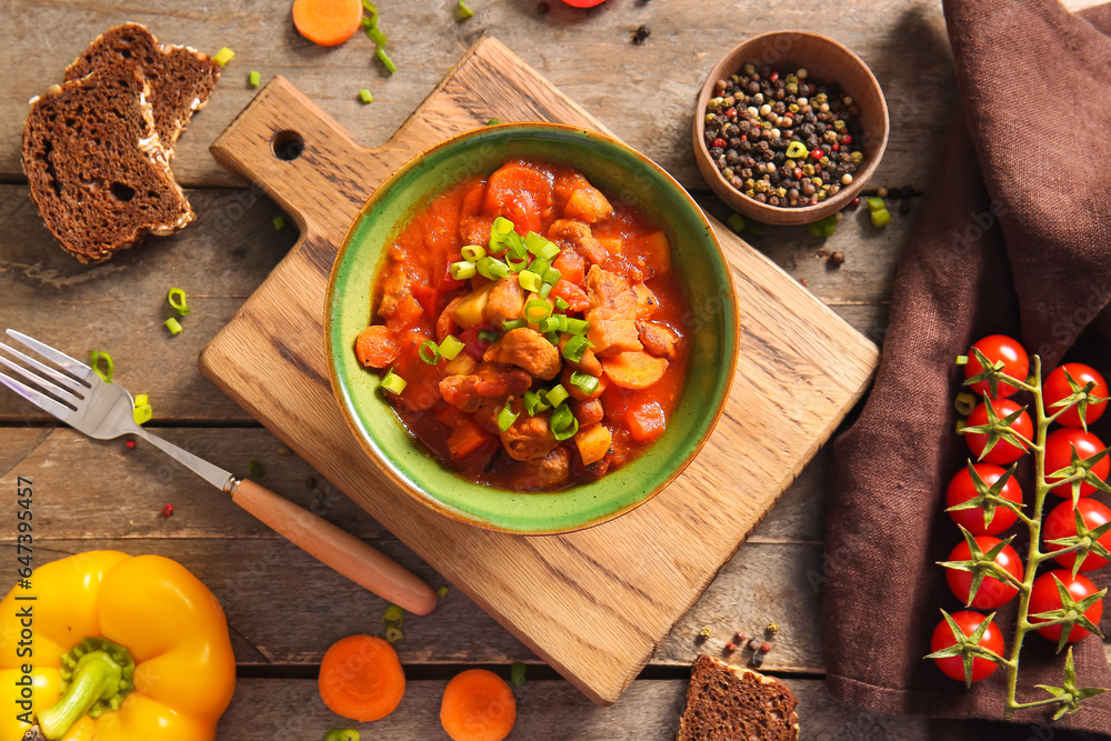 Bowl of tasty beef stew and ingredients on wooden background