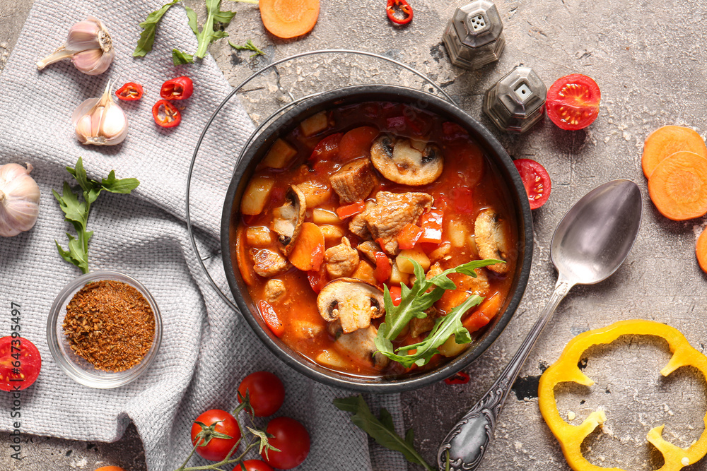 Bowl of tasty beef stew and ingredients on grey background