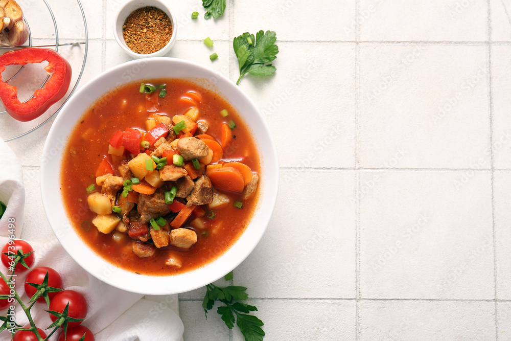 Bowl of tasty beef stew, spices and vegetables on white tile background