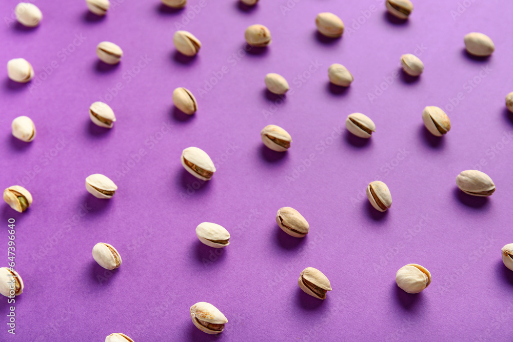 Tasty pistachio nuts on purple background