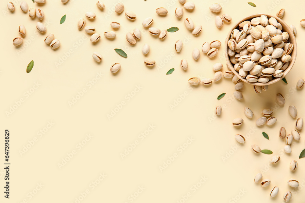 Bowl with tasty pistachio nuts and leaves on yellow background