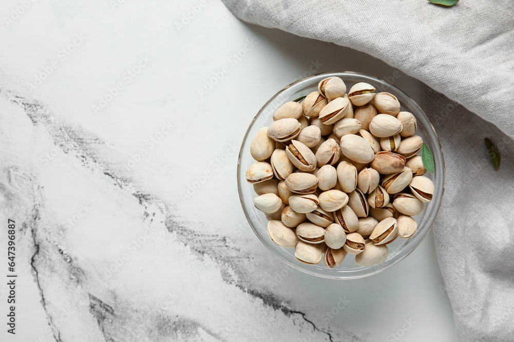 Glass bowl with tasty pistachio nuts on white background