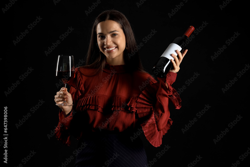 Young woman with glass and bottle of wine on black background