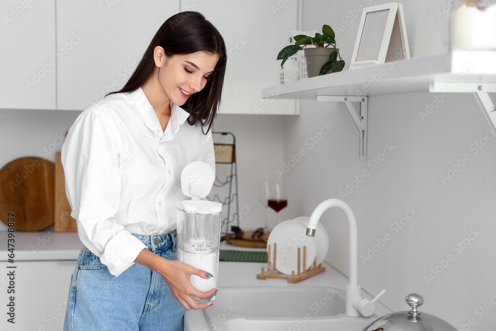 Young woman with water filter jug in kitchen