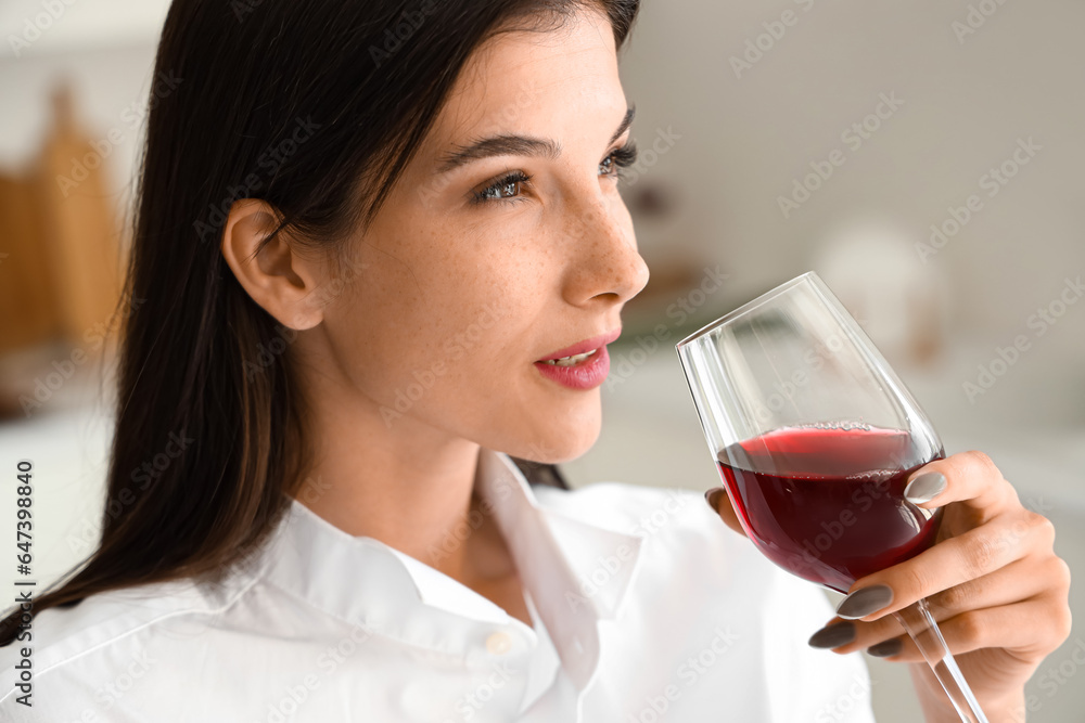 Young woman with glass of wine in kitchen, closeup