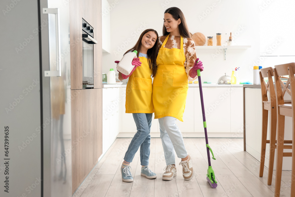 Happy mother with her little daughter hugging while cleaning in kitchen