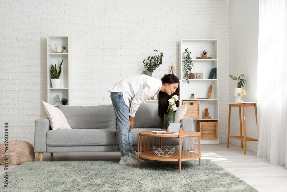 Beautiful young Asian woman with vase of flowers in living room