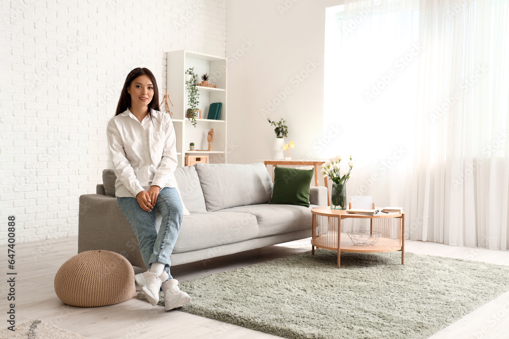 Beautiful young Asian woman sitting on sofa in living room