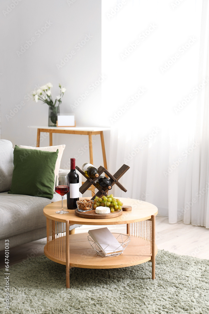 Stylish living room interior with stand of wine bottles and snacks on table