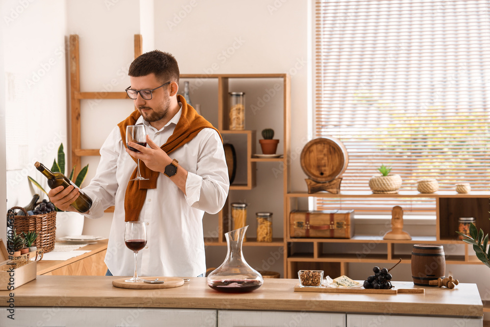 Young sommelier with bottle and glass of wine in kitchen at home