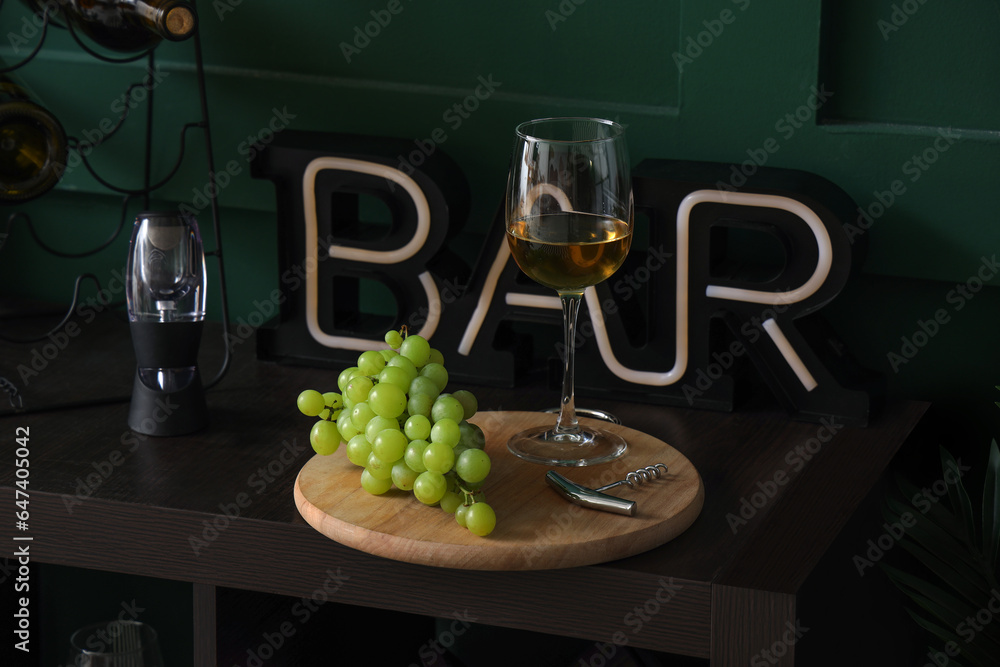 Board with glass of tasty wine and grapes on table, closeup