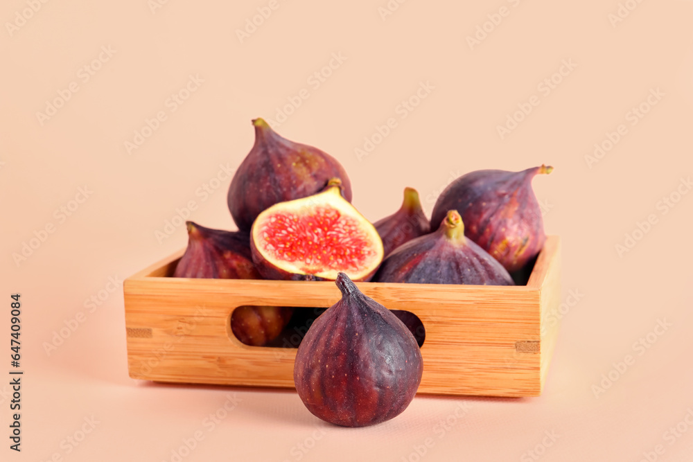 Wooden box with fresh juicy cut figs on pale pink background