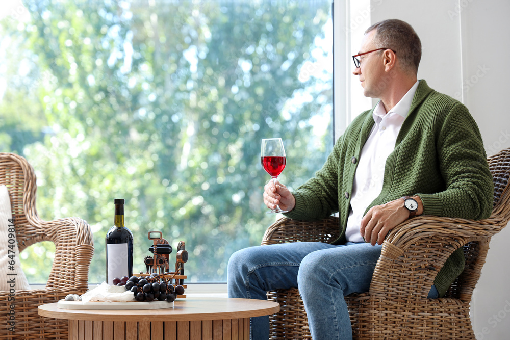 Mature man with glass of red wine sitting in armchair at home