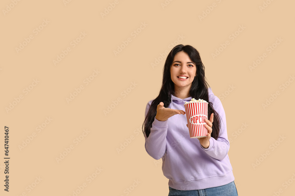 Happy young woman with bucket of popcorn on beige background