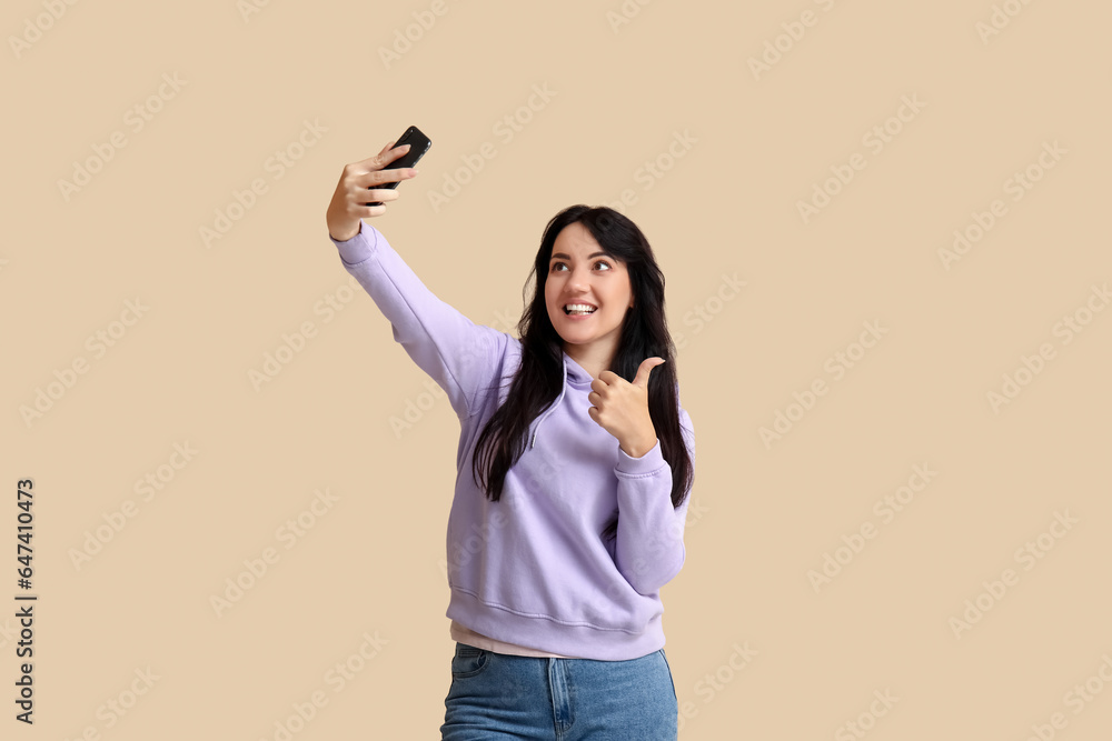 Portrait of happy young brunette taking selfie on beige background