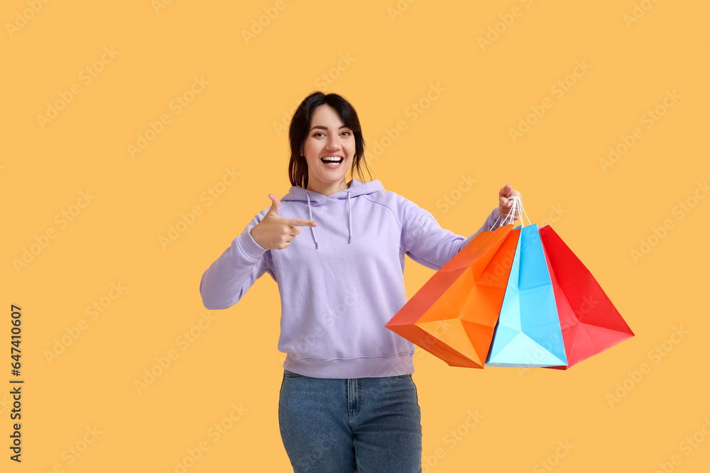 Beautiful happy woman with shopping bags on yellow background