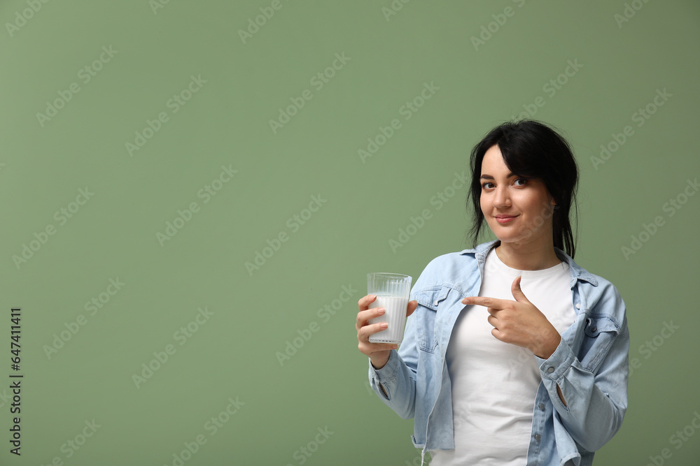 Pretty young woman with glass of milk on green background