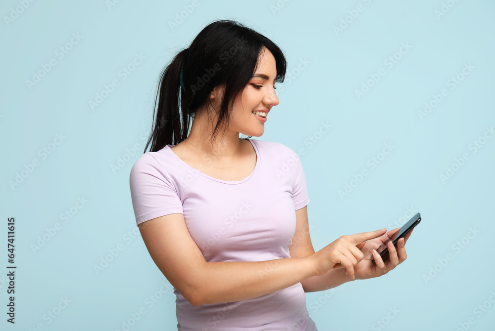 Portrait of happy young brunette with phone on blue background