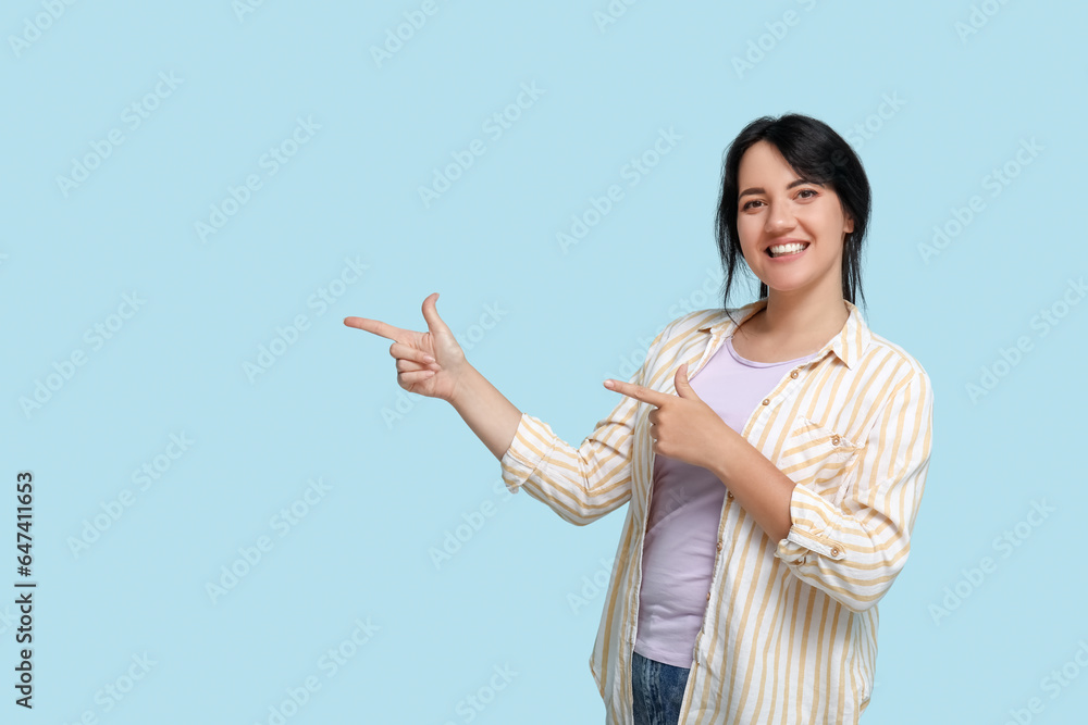 Portrait of happy young brunette pointing at something on blue background