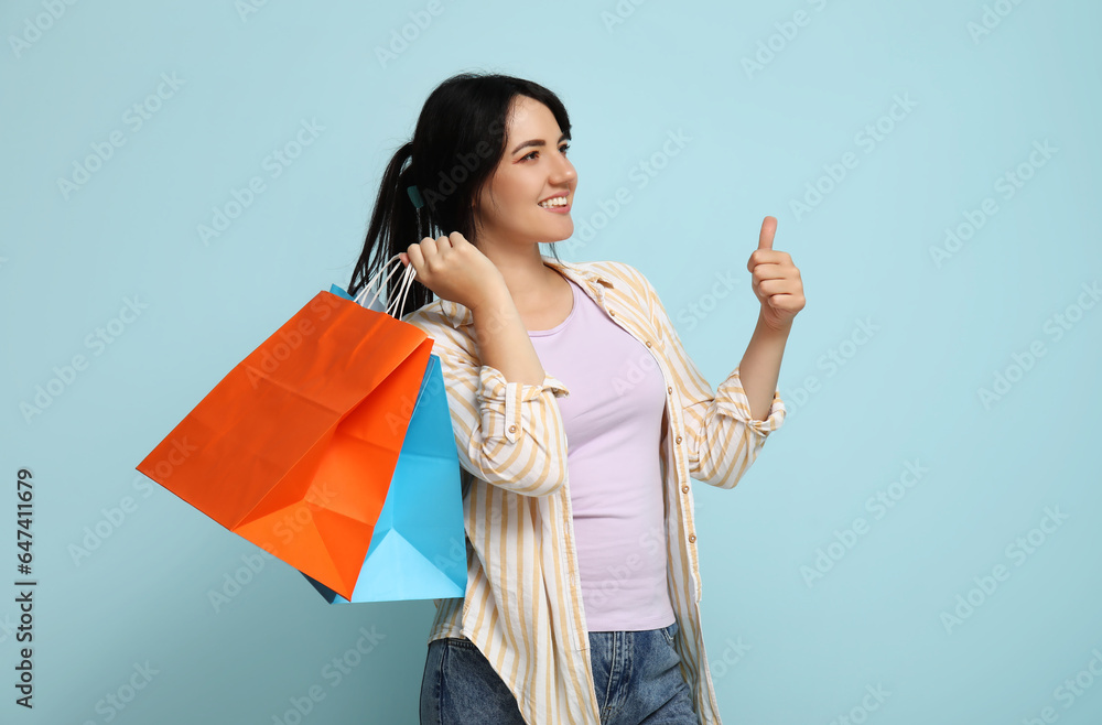 Beautiful happy woman with shopping bags showing thumb-up on blue background