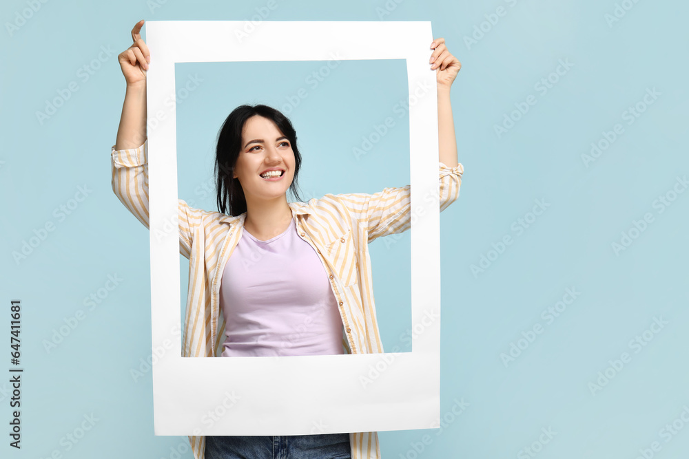 Portrait of happy young brunette with frame on blue background