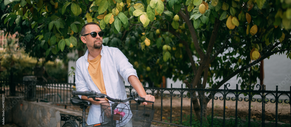 A young man with a bicycle on a green street with private houses. Eco-friendly transport.  Green mob