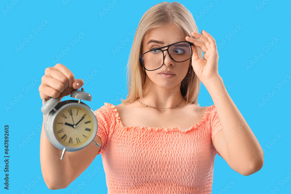 Stressed young woman with alarm clock on blue background. Deadline concept