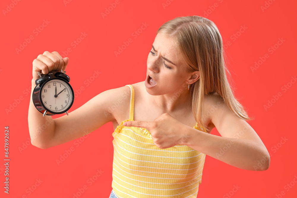 Stressed young woman pointing at alarm clock on red background. Deadline concept