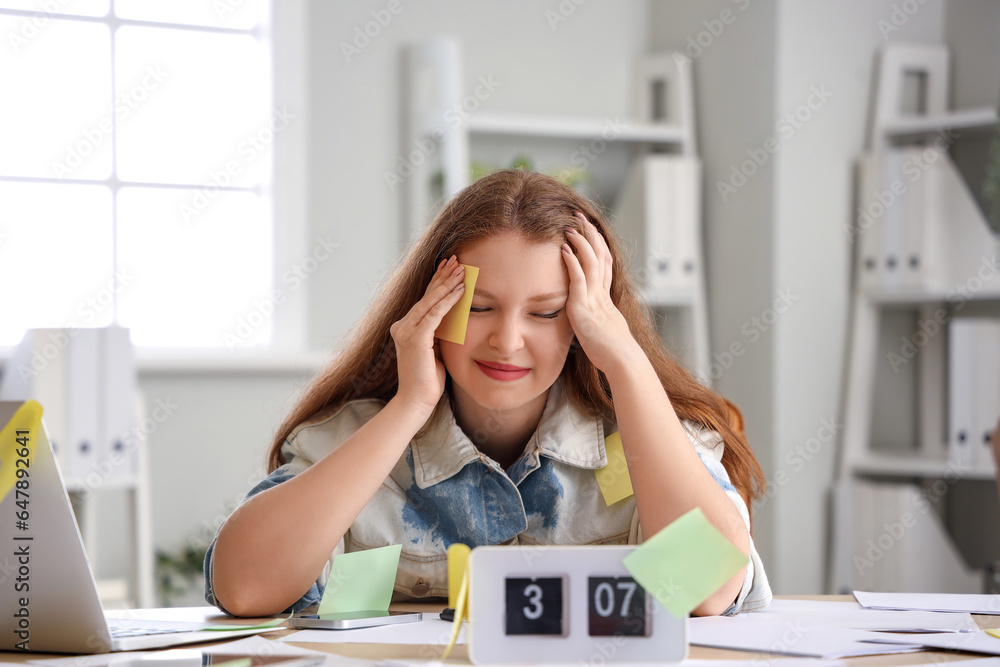 Stressed young businesswoman with sticky notes working under deadline in office