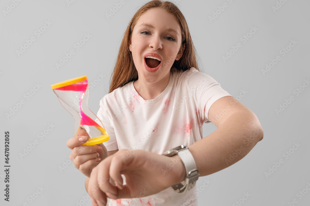 Shocked young woman with hourglass and wristwatch on grey background. Deadline concept