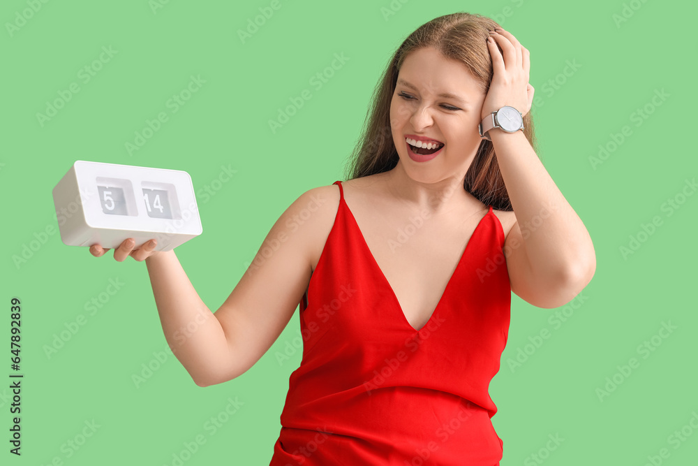 Stressed young woman with clock on green background. Deadline concept