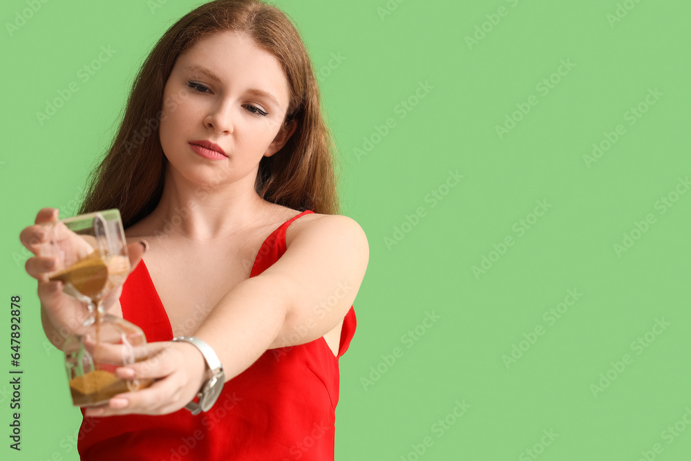 Young woman with hourglass on green background, closeup. Deadline concept