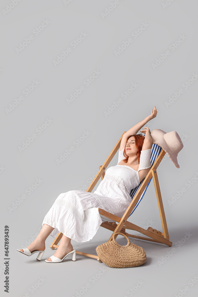 Young woman relaxing in deck chair on light background