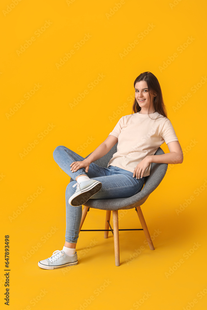 Young woman sitting in armchair on yellow background