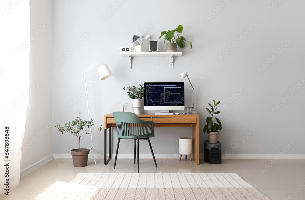 Interior of light office with programmers workplace, shelf and houseplants