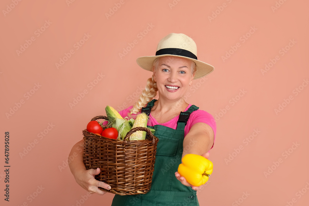 Mature female farmer with wicker basket full of different ripe vegetables on orange background