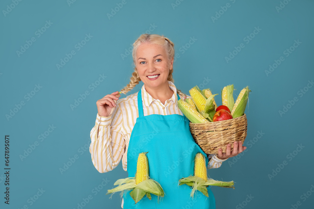 Mature female farmer with wicker basket full of different ripe vegetables on blue background