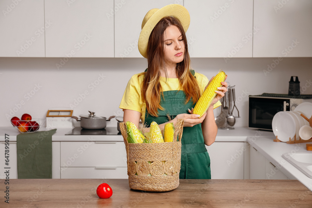 Beautiful young female farmer with wicker basket full of ripe corn cobs in kitchen