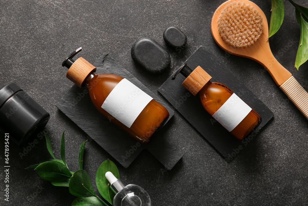 Bottles of shampoo, brush, spa stones and cosmetic products on black background