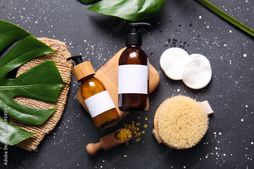 Bottles of shampoo, sea salt, brush and cotton pads on black background