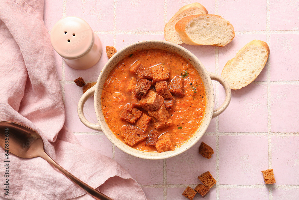 Pot of tasty cream soup with croutons and bread on pink tile background