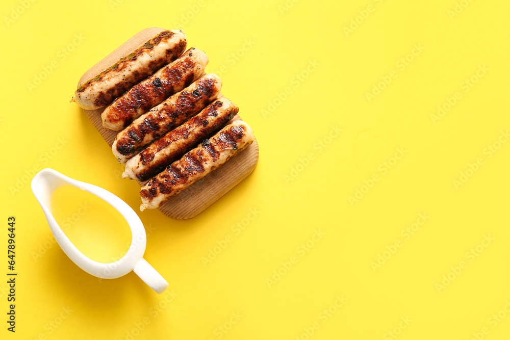 Wooden board of tasty grilled sausages and oil on yellow background