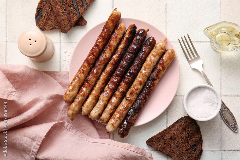 Plate of tasty grilled sausages on white tile background